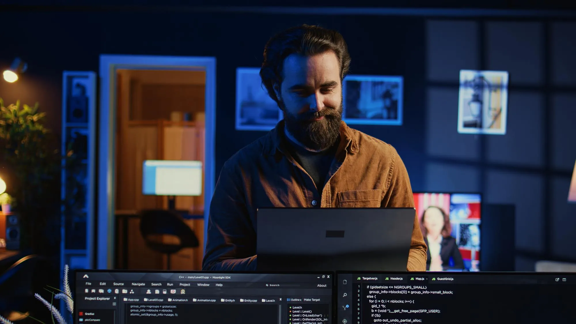 Ontwikkelaar lacht naar zijn laptop, met codeeditors op twee monitoren voor hem in een schemerig thuiskantoor