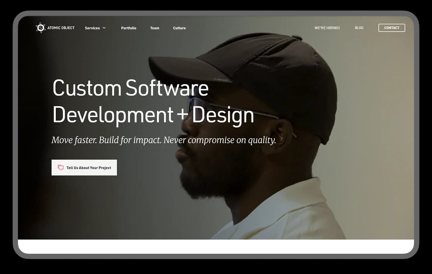 Atomic Object homepage hero: "Custom Software Development + Design" over a photo of a bearded man in a cap, with a Tell Us About Your Project button