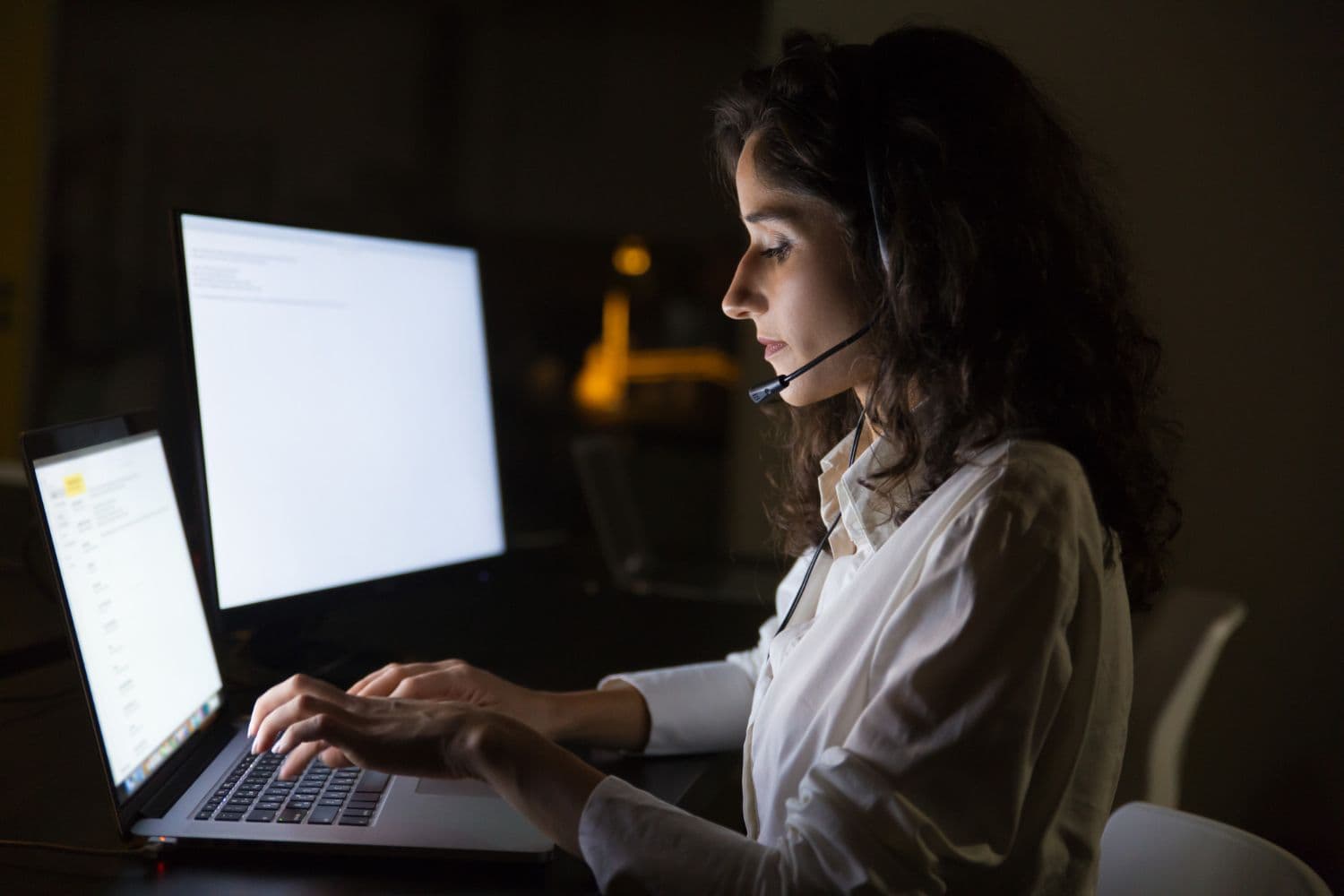 Vrouw met een headset die typt op een laptop in een donker kantoor, als beeld van klantenservice en feedbackgesprekken